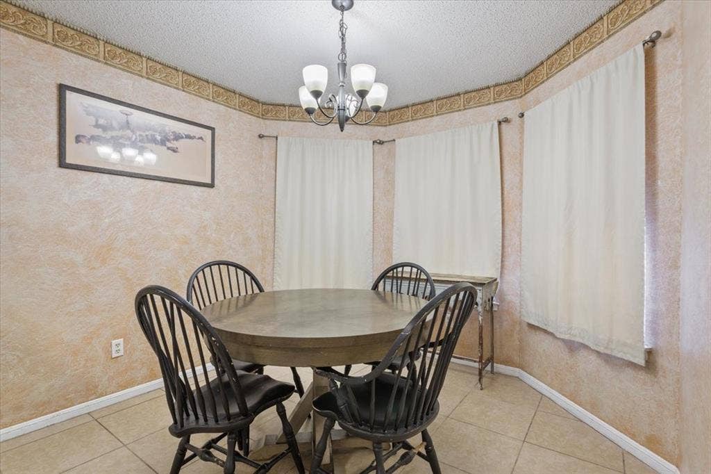 Bay window with multiple panels, tiled flooring, textured wall finish, decorative ceiling border, and a five-light chandelier