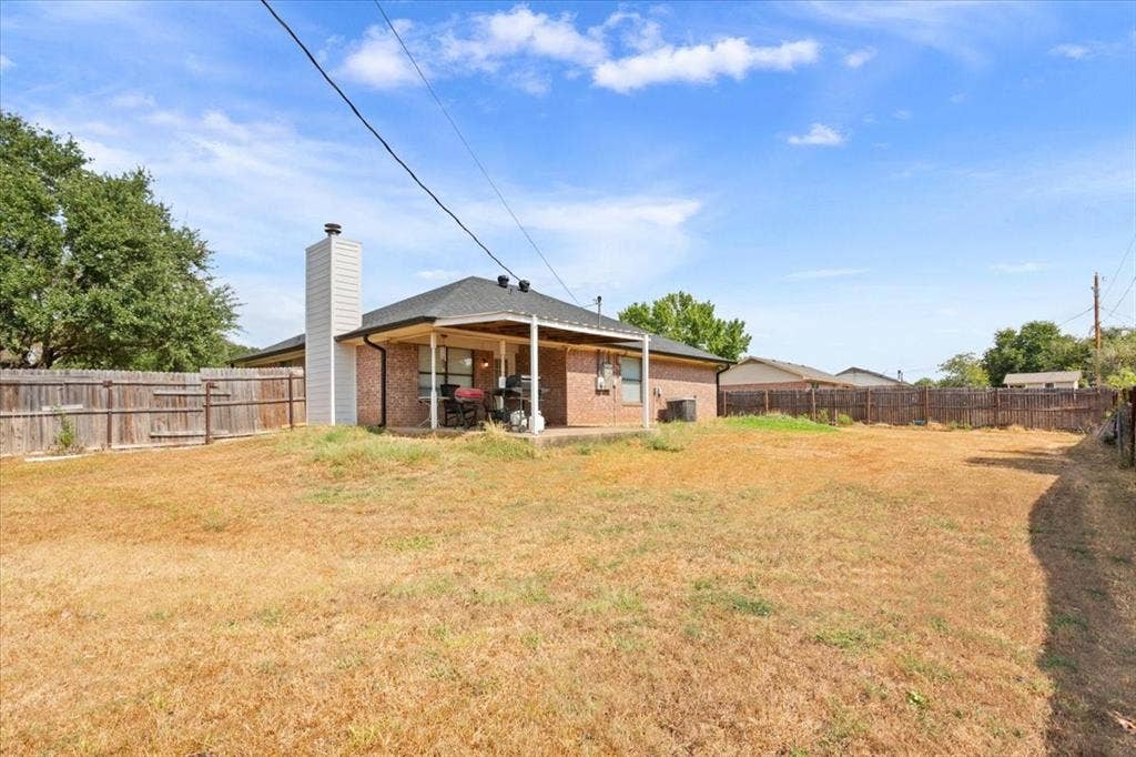 Expansive backyard featuring a covered patio, brick exterior, wood-paneled chimney, and full perimeter fencing