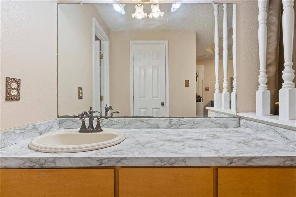 Built-in vanity with a patterned countertop, integrated oval sink, and wood-finish cabinetry
