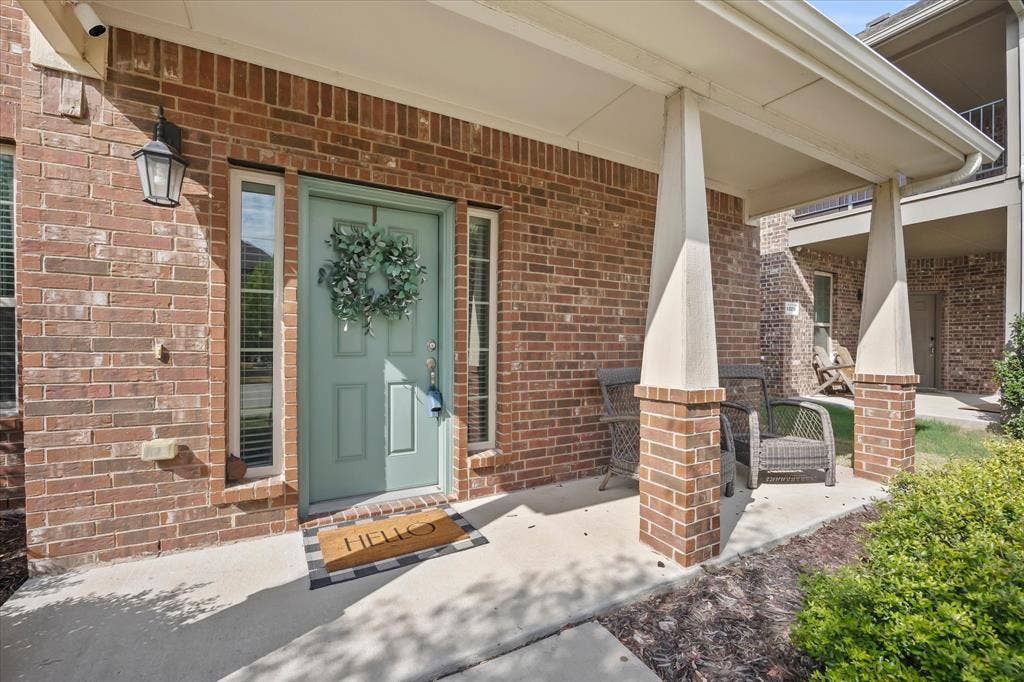 1225 Honeywood Lane, Royse City, TX 75189 Brick exterior with a covered porch, featuring a panel-style front door, two sidelight windows, and an exterior wall lantern