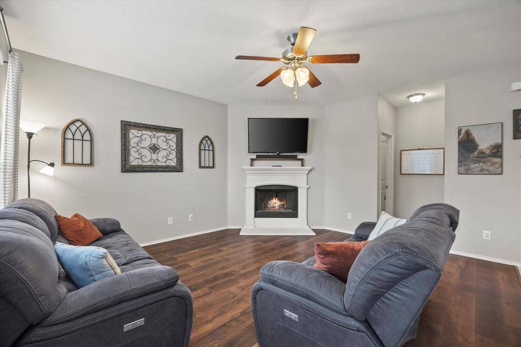 1225 Honeywood Lane, Royse City, TX 75189 Wood-finish flooring, central fireplace with white mantel, ceiling fan with integrated lighting, recessed wall niche, and light gray wall paint throughout