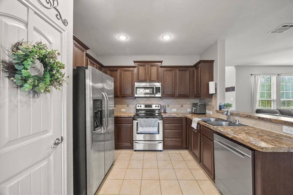 1225 Honeywood Lane, Royse City, TX 75189 U-shaped kitchen with wood-finish cabinetry, tile flooring, stainless steel appliances, and a double basin sink