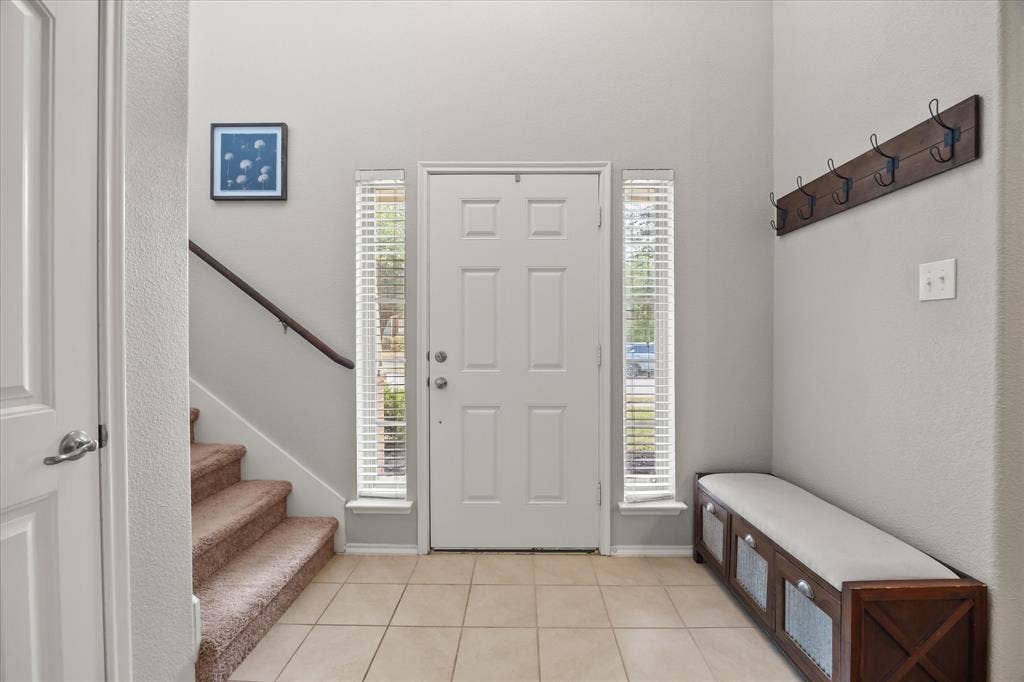 1225 Honeywood Lane, Royse City, TX 75189 Foyer featuring a paneled entry door, side light windows with blinds, tiled flooring, and a carpeted staircase with a wood handrail