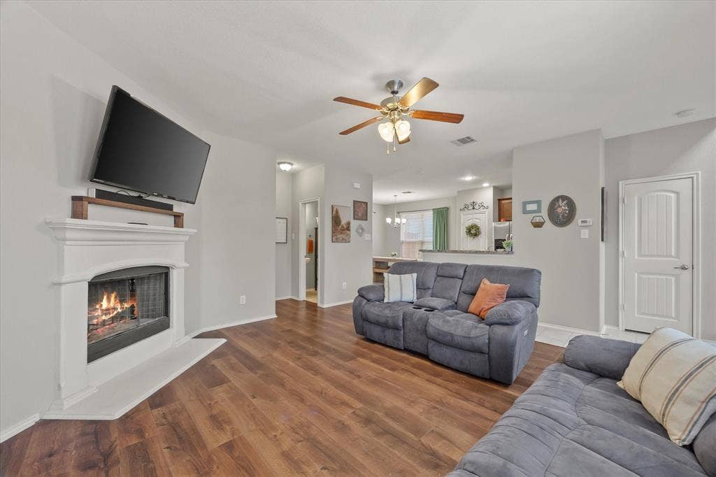 1225 Honeywood Lane, Royse City, TX 75189 Living area with wood-finish flooring, a white mantel fireplace, and a ceiling fan with integrated lighting