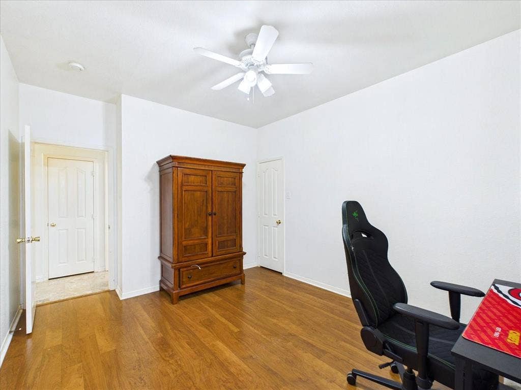 Spacious bedroom showcasing refinished wood flooring, ceiling fan with integrated lighting, and abundant natural light