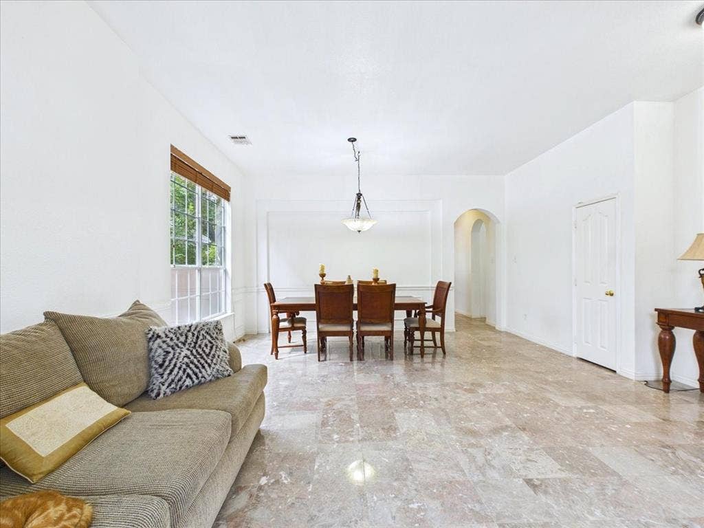 Polished light-toned tile flooring throughout, dining area with a chandelier and wall trim, and an arched doorway