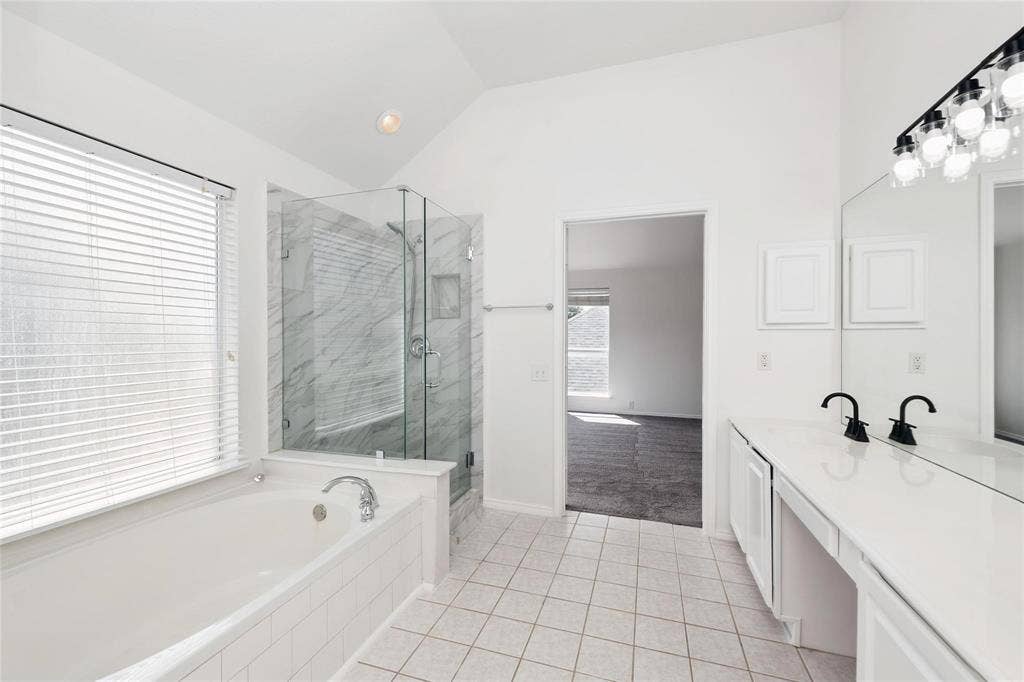 11443 Waterford Lane, Frisco, TX 75035 Soaking tub, glass-enclosed shower with tiled walls, dual vanity with black fixtures, vaulted ceiling, and tiled flooring