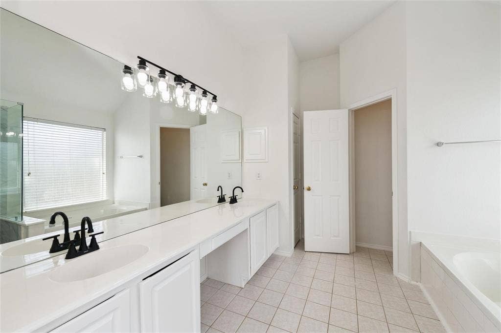 11443 Waterford Lane, Frisco, TX 75035 Double vanity with undermount sinks and matte black faucets, extensive counter space, full-width wall mirror, and a built-in tub with a window