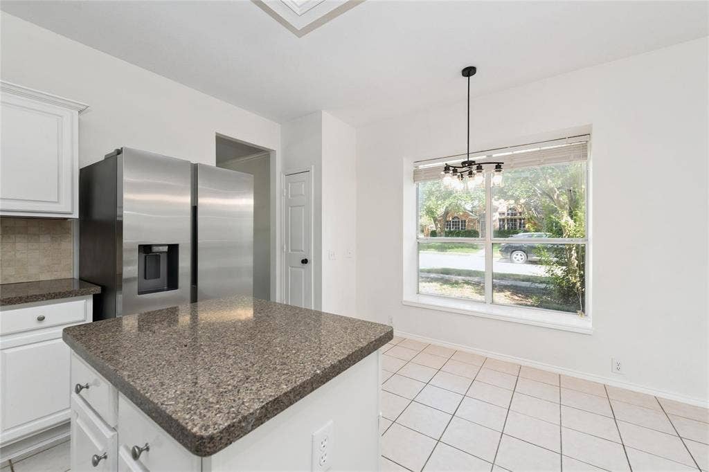 11443 Waterford Lane, Frisco, TX 75035 Kitchen featuring an island with stone countertops, white cabinetry, stainless steel refrigerator, tile backsplash, and tile flooring