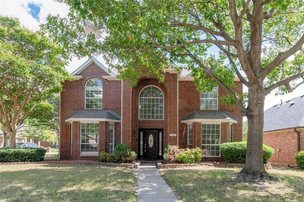 11443 Waterford Lane, Frisco, TX 75035 Brick exterior with arched and bay windows, a dark wood-finish entry door, and mature landscaping