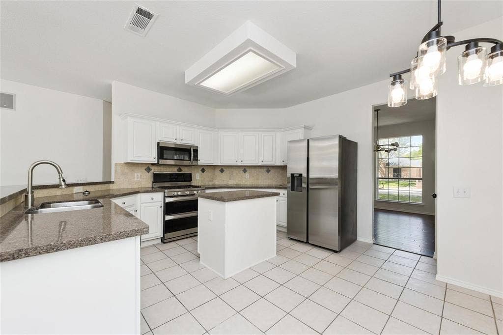 11443 Waterford Lane, Frisco, TX 75035 White cabinetry with stainless steel appliances, granite countertops, kitchen island, and tiled flooring