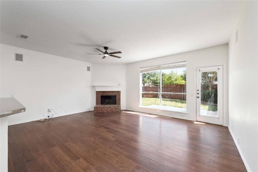 11443 Waterford Lane, Frisco, TX 75035 Spacious room featuring wood-finish flooring, a brick fireplace with mantel, a ceiling fan, and backyard access via a glass-paneled door