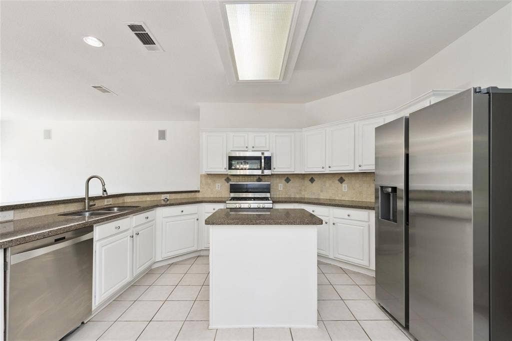 11443 Waterford Lane, Frisco, TX 75035 Kitchen featuring white cabinetry, stainless steel appliances, a center island, stone-finish countertops, and a tiled backsplash