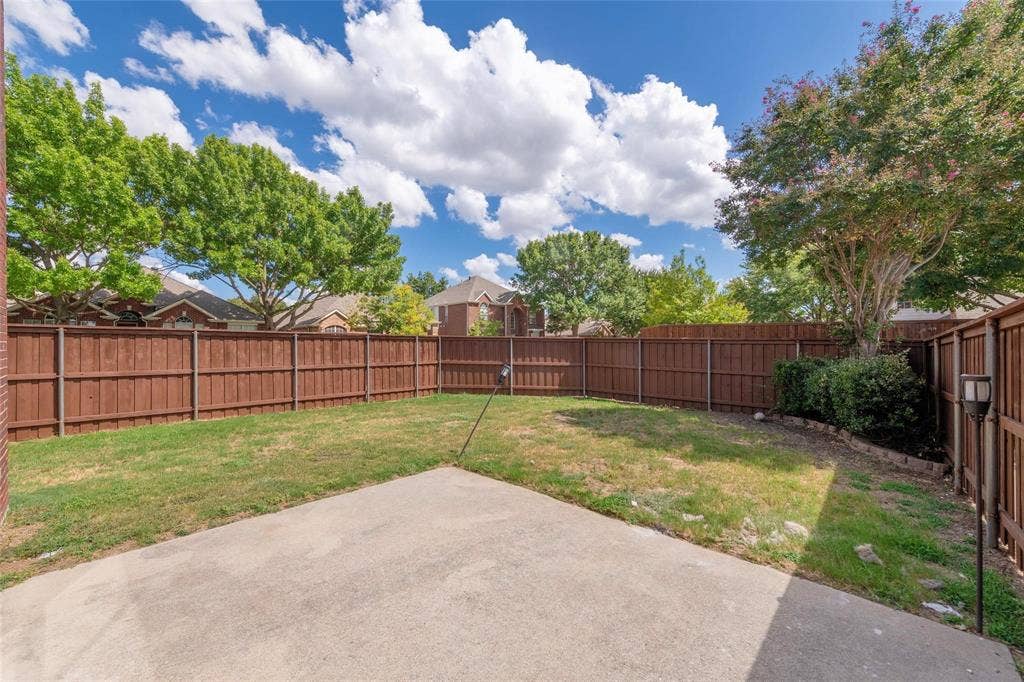 11443 Waterford Lane, Frisco, TX 75035 Expansive fenced backyard with a concrete patio, mature trees, and a landscaped perimeter