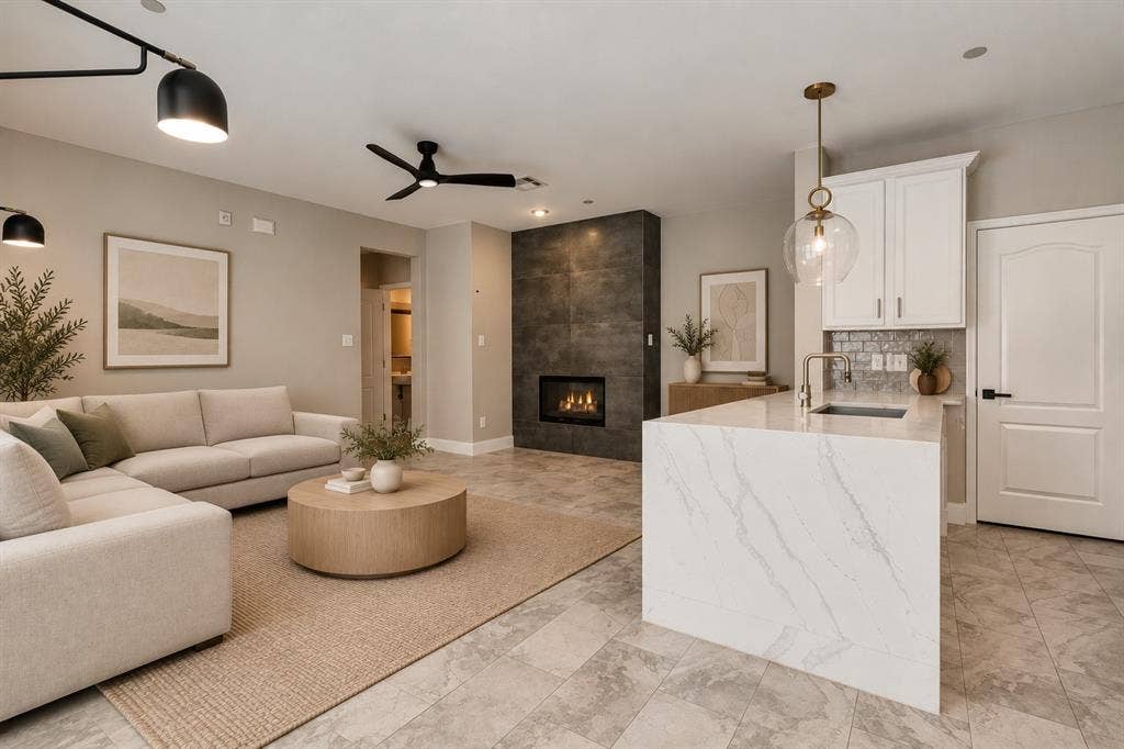 6854 Cortona Lane, Frisco, TX 75034 Integrated living space featuring a tiled fireplace with a built-in firebox, a kitchen island with a waterfall countertop, white cabinetry with a subway tile backsplash, and overhead lighting fixtures