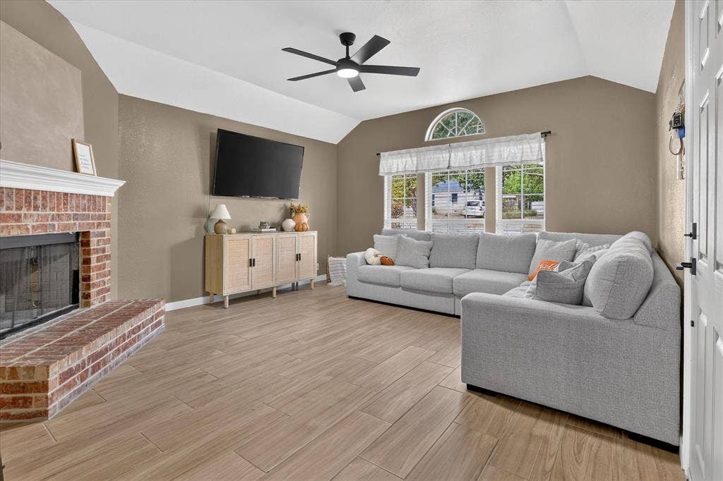 5413 Cornell Avenue, River Oaks, TX 76114 Vaulted ceiling with a black ceiling fan, brick fireplace with a white mantel, wood-finish tile flooring, and a large window with an arched transom