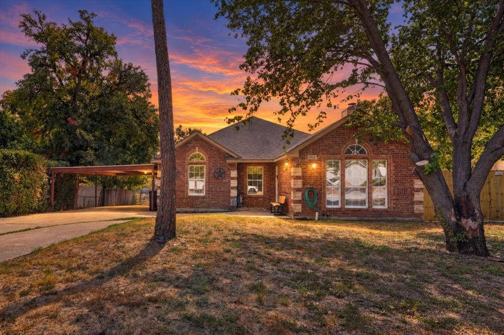 5413 Cornell Avenue, River Oaks, TX 76114 Brick exterior with arched windows, mature trees, and a concrete driveway leading to a carport