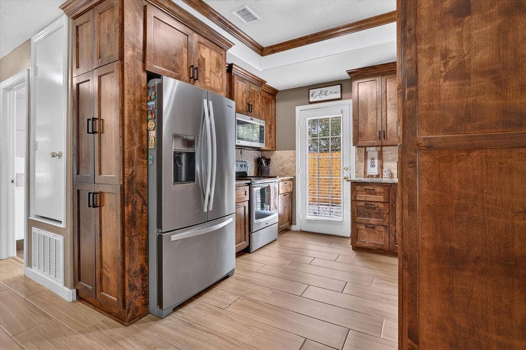5413 Cornell Avenue, River Oaks, TX 76114 Wood-finish cabinetry, stainless steel appliances, tiled backsplash, light-toned flooring, and a glass-paned exterior door