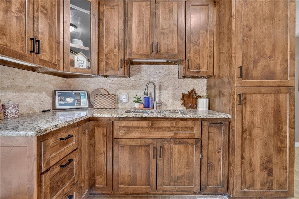 5413 Cornell Avenue, River Oaks, TX 76114 Wood-finish cabinetry with black hardware, light-toned stone countertops, and a tile backsplash