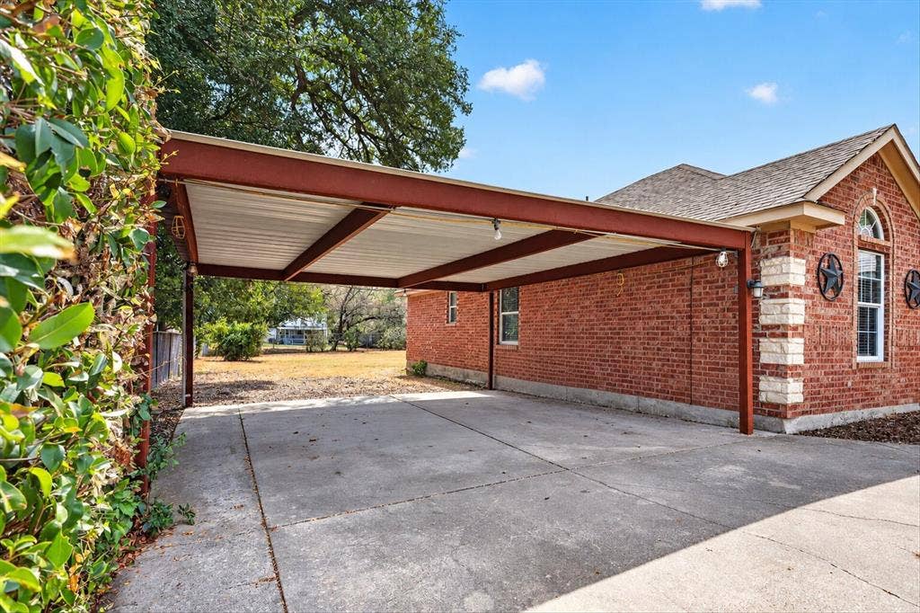 5413 Cornell Avenue, River Oaks, TX 76114 Attached carport structure, concrete driveway, brick exterior with stone accents, arched window, and exterior wall sconces
