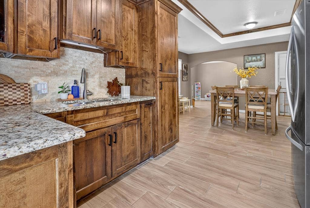 5413 Cornell Avenue, River Oaks, TX 76114 Kitchen featuring wood cabinetry, granite countertops, a stainless steel sink with a gooseneck faucet, and a stone-finish backsplash