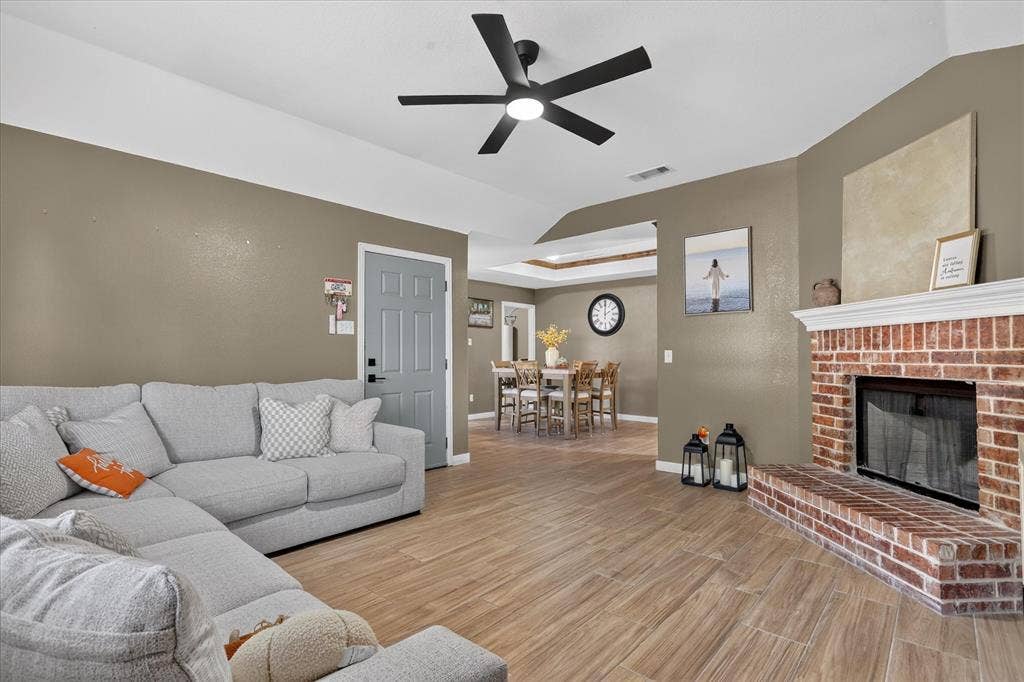 5413 Cornell Avenue, River Oaks, TX 76114 Wood-finish flooring, brick fireplace with mantel, ceiling fan with integrated lighting, and a tray ceiling detail