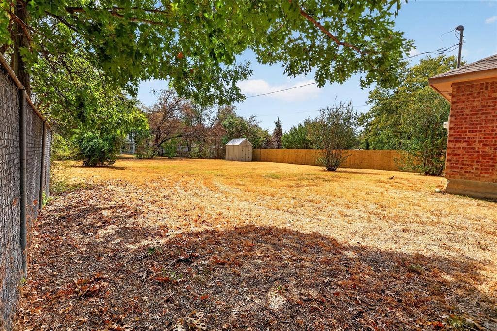5413 Cornell Avenue, River Oaks, TX 76114 Expansive yard featuring a chain-link fence, a wooden privacy fence, mature trees, and a storage shed