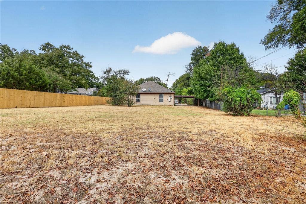 5413 Cornell Avenue, River Oaks, TX 76114 Expansive open lot with a tan brick exterior, a new wood-panel fence, a covered carport, and mature perimeter trees