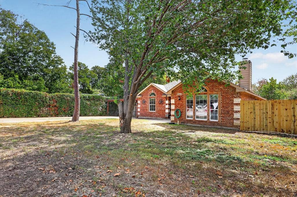 5413 Cornell Avenue, River Oaks, TX 76114 Brick exterior with arched windows, a prominent chimney, and a wooden privacy fence