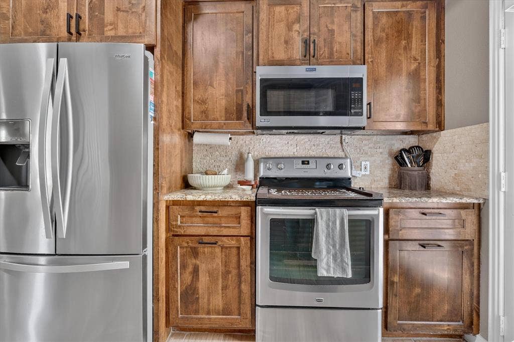 5413 Cornell Avenue, River Oaks, TX 76114 Stainless steel refrigerator, coordinating stainless steel range, built-in stainless steel microwave, wood-finish cabinetry, and stone-look countertops
