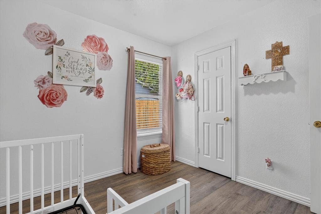 5413 Cornell Avenue, River Oaks, TX 76114 Wood-finish flooring with white baseboards, a white paneled door with a brass-finish knob, and a window with horizontal blinds