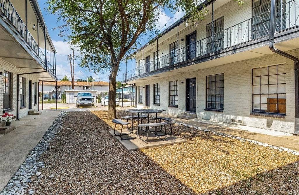 5317 Junius Street, #214, Dallas, TX 75214 Two-story building featuring white brick facade, black wrought iron railings, black window frames, and a central courtyard