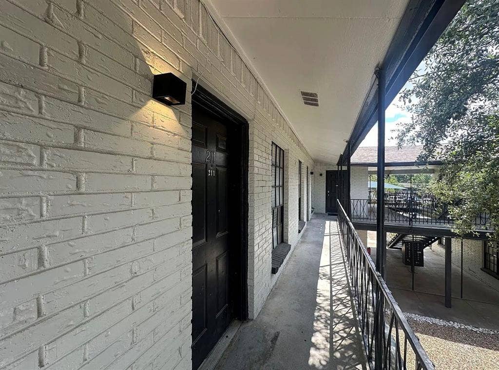 5317 Junius Street, #214, Dallas, TX 75214 Painted brick exterior with a black entrance door, black outdoor wall light, dark metal railing, and concrete walkway