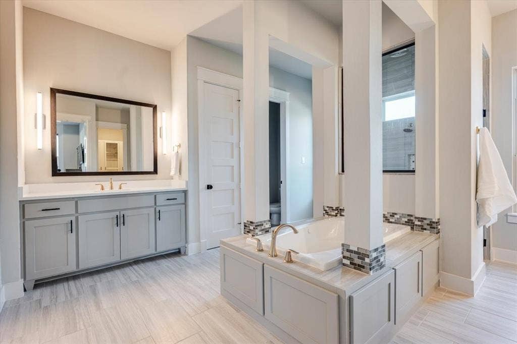 4102 Parkview Boulevard, Celina, TX 75009 Wood-look tile flooring, built-in soaking tub with tile surround, dual vanity with shaker-style cabinetry, rectangular undermount sink, and wall-mounted sconce lighting