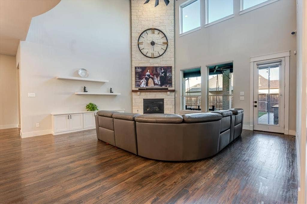 4102 Parkview Boulevard, Celina, TX 75009 Spacious living area featuring wood-finish flooring, a stone-clad fireplace with a mantel, built-in shelving, and large windows with transom panels