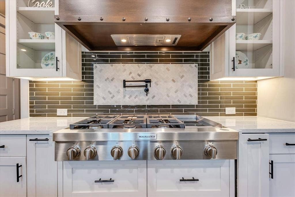 4102 Parkview Boulevard, Celina, TX 75009 Stainless steel gas range with a wood-finish hood, solid surface countertops, glass-front upper cabinetry, and a subway tile backsplash