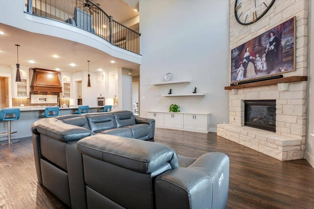 4102 Parkview Boulevard, Celina, TX 75009 Two-story ceiling, stone-surround fireplace with wood mantel, wood-finish flooring, built-in cabinetry, and a second-story balcony with metal railing