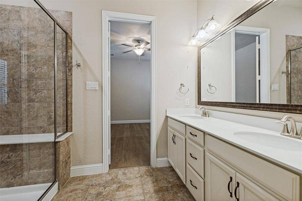 Dual vanity, decorative framed mirror, attached wall sconce lighting, and a walk-in shower with tiled walls and a glass enclosure