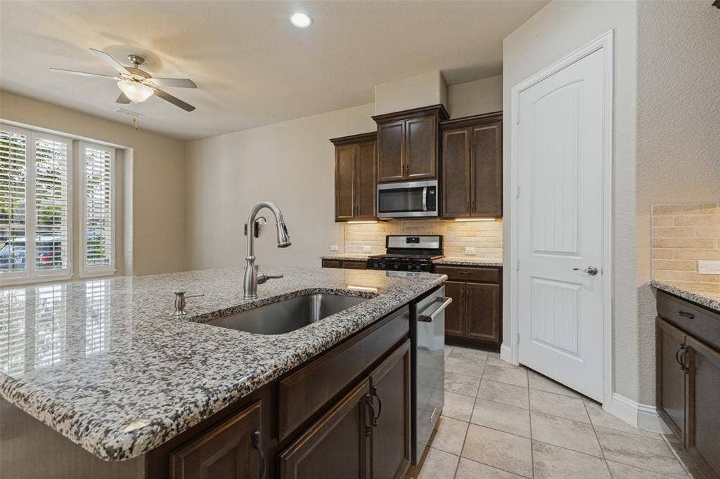 Kitchen island with granite countertop and undermount sink, stainless steel appliances with gas cooktop range, and walk-in pantry