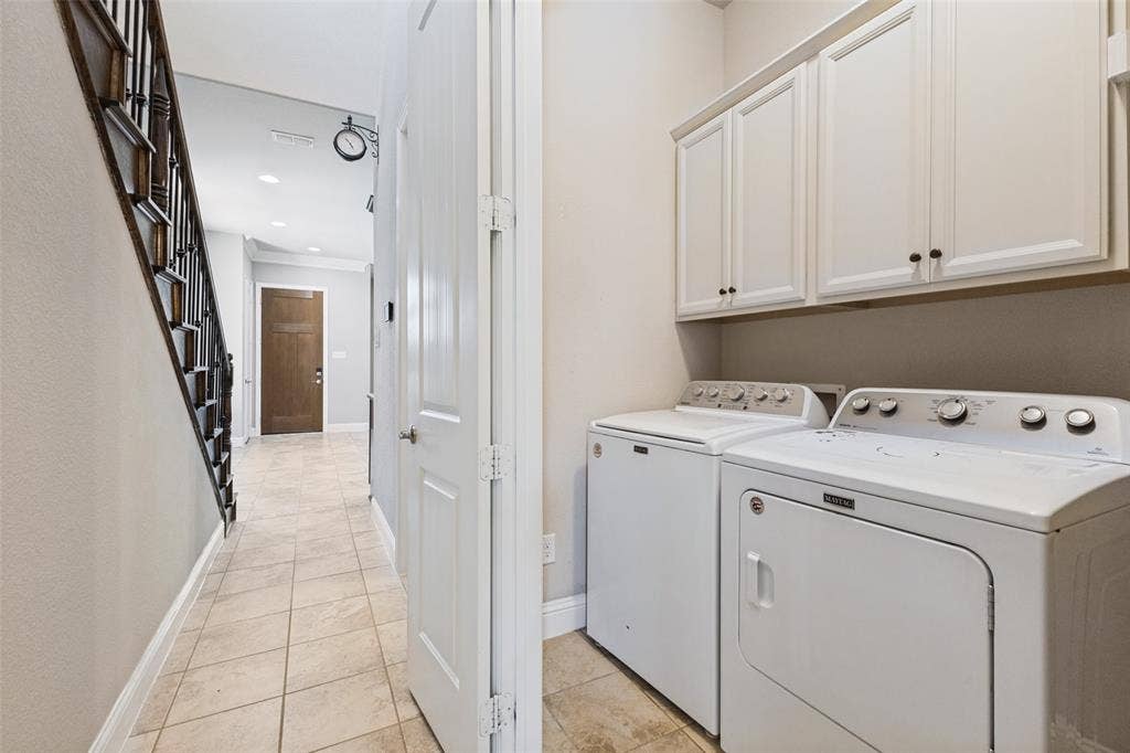Laundry area with white cabinetry, tile flooring, and a dark wood-finish staircase