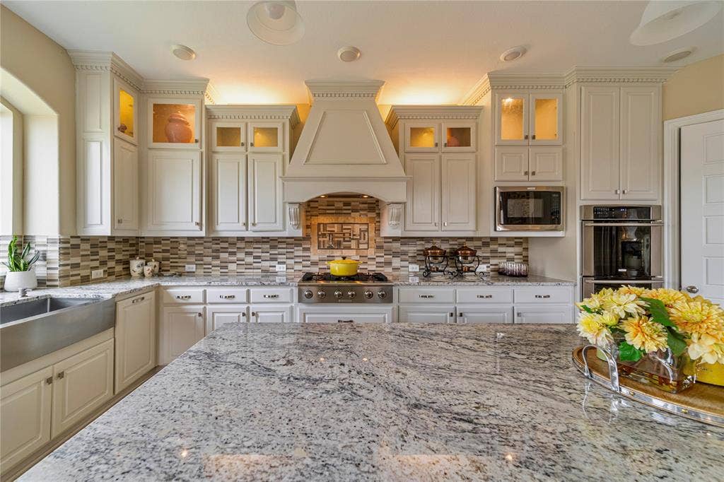 13018 Seattle Slew Street, Frisco, TX 75035 Granite countertops with an integrated island, white cabinetry with crown molding, stainless steel appliances, and a mosaic tile backsplash