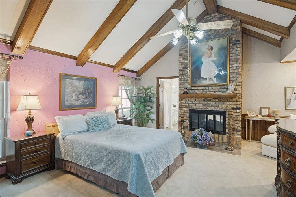 Vaulted ceiling with wood beams, brick fireplace with mantel, ceiling fan, and carpeted flooring