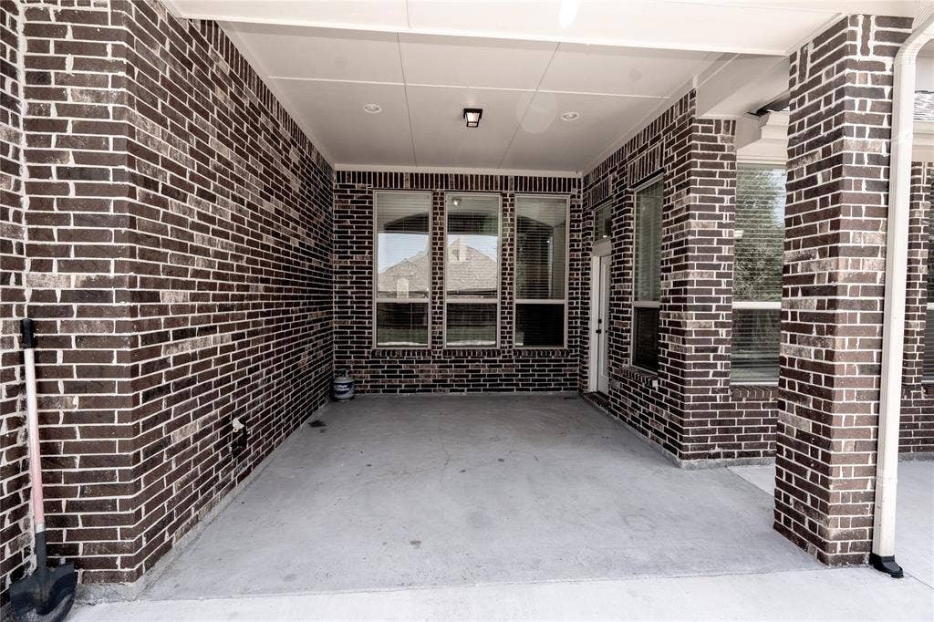 Covered concrete patio featuring dark brick walls, multiple windows, a white door, and a recessed ceiling light