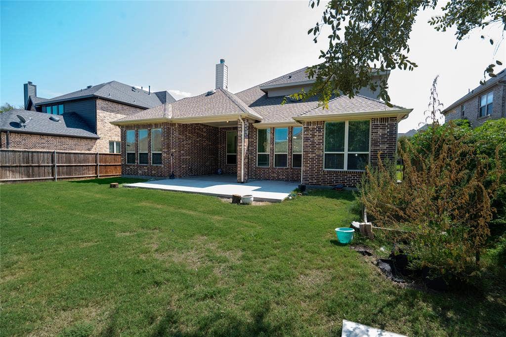 Expansive green lawn with a covered patio, brick exterior, multiple windows, and a wood privacy fence