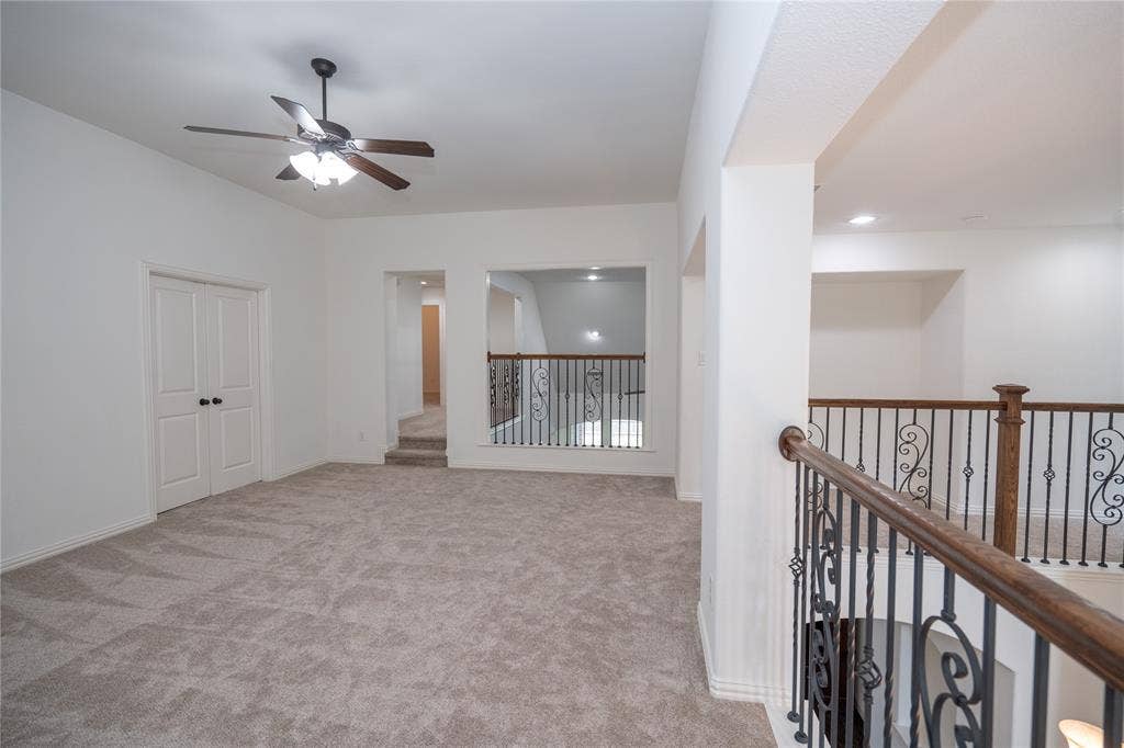 Carpeted open area with ceiling fan, recessed lighting, and wrought iron balusters