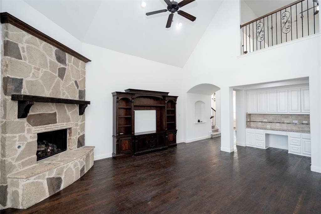 Spacious living area featuring a stone-clad fireplace with mantel, dark wood-finish flooring, and a built-in entertainment center