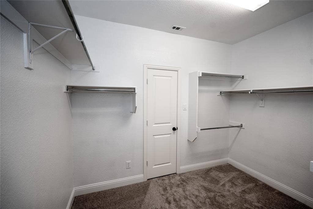 Wall-mounted shelving with integrated hanging rods, carpeted flooring, white trim, and overhead lighting
