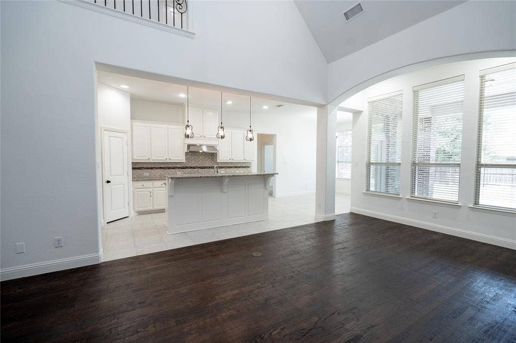 Vaulted ceiling with decorative iron railing, dark wood-finish flooring, and multiple large windows with blinds