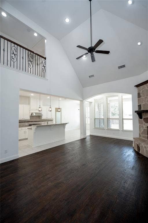Vaulted ceiling with a ceiling fan, dark wood-finish flooring, stone fireplace, and an open-concept kitchen with a breakfast bar