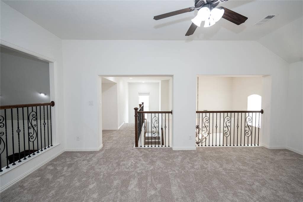 Vaulted ceiling with a ceiling fan, carpeted flooring, and decorative wrought iron railings